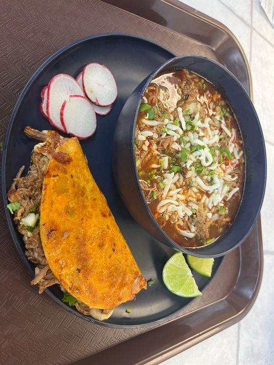 Birria ramen in rich broth topped with cheese and cilantro, served with a quesabirria and lime