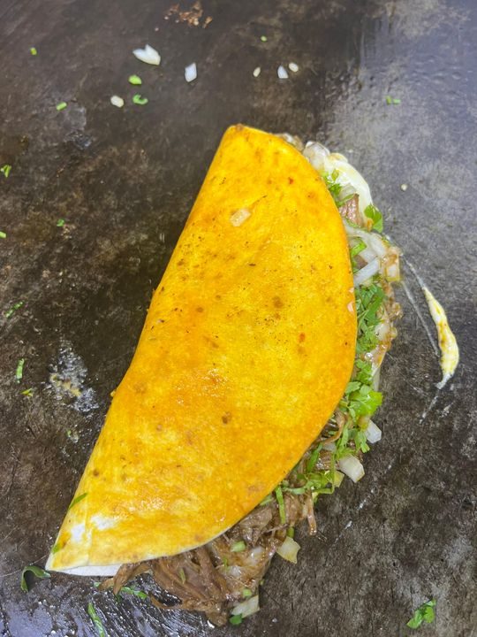 Quesabirria on the griddle with consomé-dipped tortilla, onion and cilantro